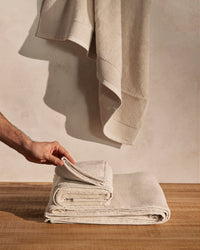 A person's hand holding one of the towels of the ONSEN Oatmeal Plush Towel Set.