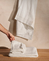 A hand holding one of the towels of the ONSEN White Plush Bath Towel Set.