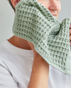 A woman cleaning her face with the Sage Waffle Face Towel.