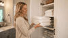 A blonde woman putting white towels in the cabinet.