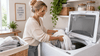 A blonde woman putting the towels in a top load washing machine.