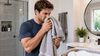 A man sniffing his own towel while in the bathroom.