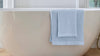 A light blue bath towel draped over a modern bathtub, complementing the bath mat vs bath rug theme.