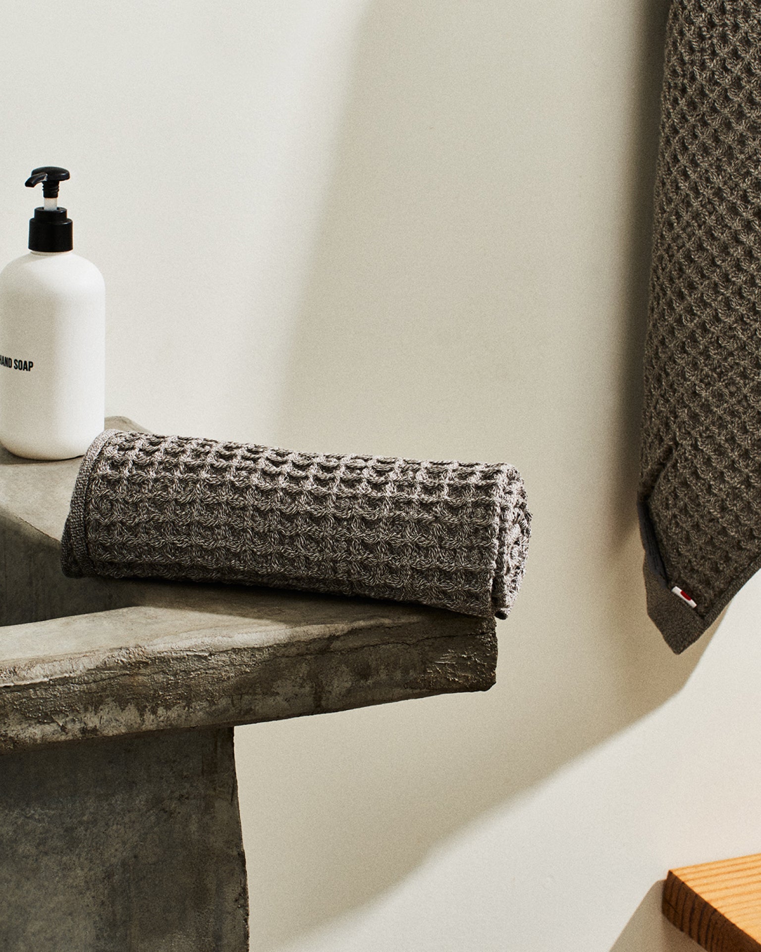 Onsen Waffle Towel  in Cinder Grey resting on the edge of the sink #color_cinder-grey