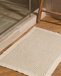 Onsen Supima cotton bath mat in cream placed on hardwood bathroom floor beside a glass shower.