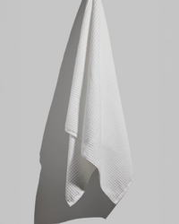 White bath towel hanging from a wall hook against a grey background.