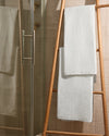 Two white bath towels draped over a wooden towel ladder beside a glass shower.