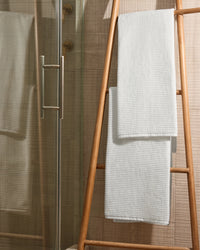 Two white bath towels draped over a wooden towel ladder beside a glass shower.