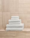 Complete white towel set neatly stacked by size on a stone bathroom ledge.