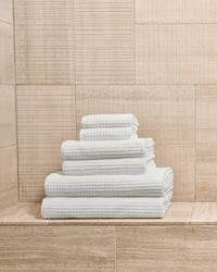 Complete white towel set neatly stacked by size on a stone bathroom ledge.