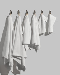 Complete white towel set hanging on wall hooks, showing bath, hand, and face towel sizes.