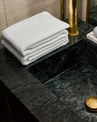 White hand towels stacked on a dark green marble countertop with brass fixtures and a gold dish.