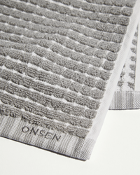 Close-up of grey fog towel showing textured weave pattern, border trim, and embroidered logo.