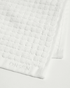 Close-up of white towel showing textured weave pattern, border trim, and embroidered logo.