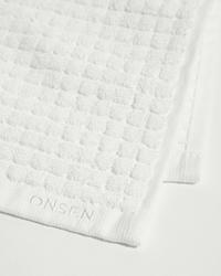 Close-up of white towel showing textured weave pattern, border trim, and embroidered logo.