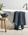 Blue towel draped over a white bathtub with a wooden stool and plant in the background