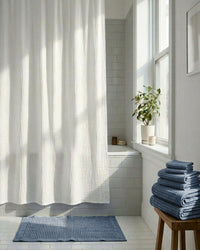 Bathroom with white shower curtain, blue towels, and a plant on a windowsill.