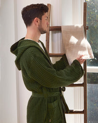 A man wearing the ONSEN Forest Waffle Bath Robe holding another waffle towel.