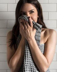 A close-up image of a woman wrapped in the ONSEN Cinder Grey Waffle Bath Sheet.