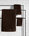 The ONSEN Brown Waffle Bath Sheet Move in set hanging on a rack.