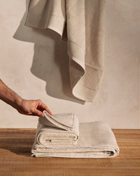 A person's hand holding one of the towels of the ONSEN Oatmeal Plush Towel Set. 