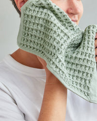 A woman cleaning her face with the Sage Waffle Face Towel. 