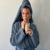 A woman wearing the ON Denim Waffle Bath Towel and Bath Robe while drinking coffee.