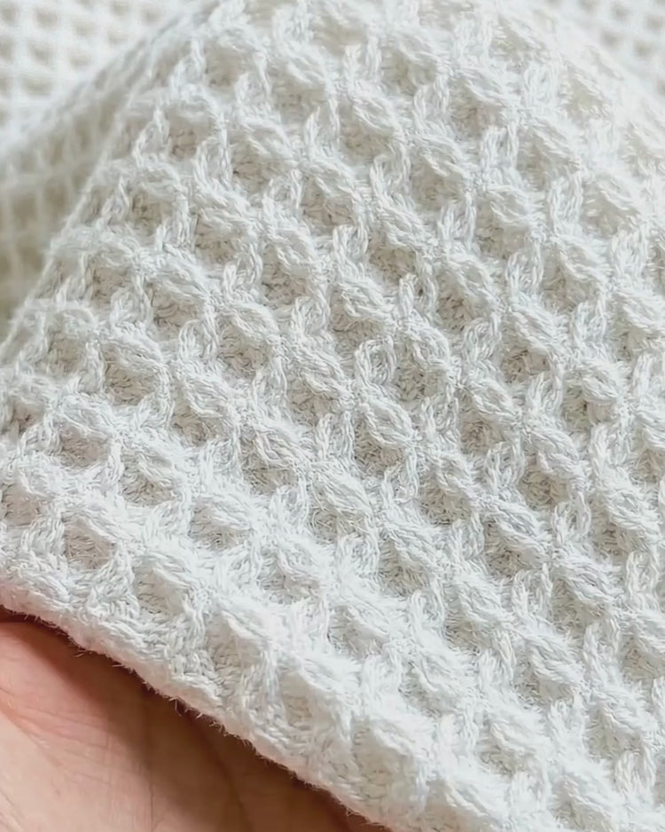 A close-up of a textured white waffle-weave bath towel being held.